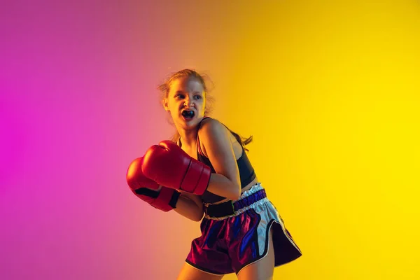 Kleine kaukasische Kickboxerin trainiert auf Gradienten-Hintergrund in Neonlicht, aktiv und ausdrucksstark — Stockfoto