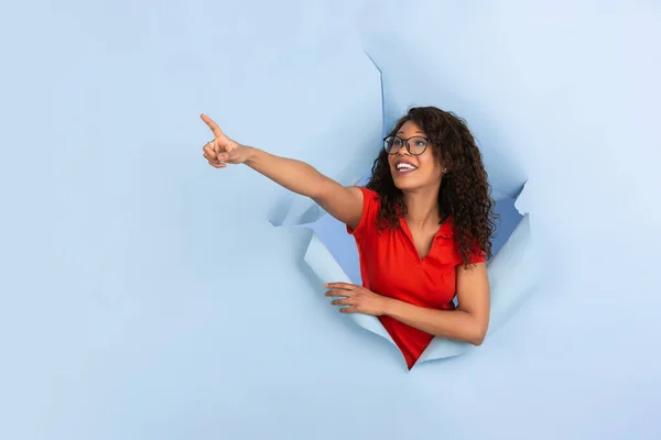 Veselá mladá žena pózuje v roztrhané modré papírové díře pozadí, emocionální a expresivní — Stock fotografie