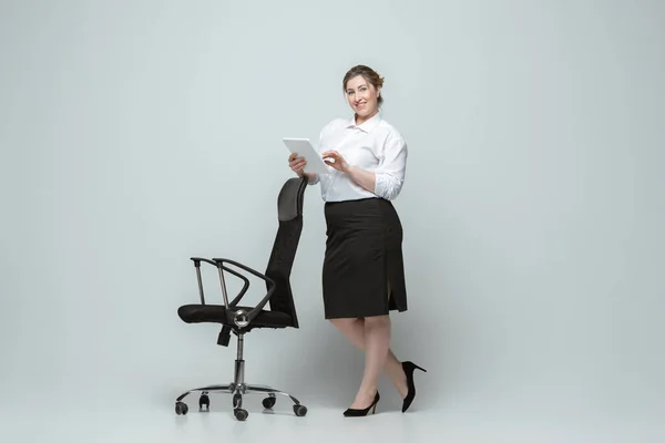 Mujer joven caucásica en traje de oficina sobre fondo gris. Personaje femenino positivo. más tamaño mujer de negocios — Foto de Stock