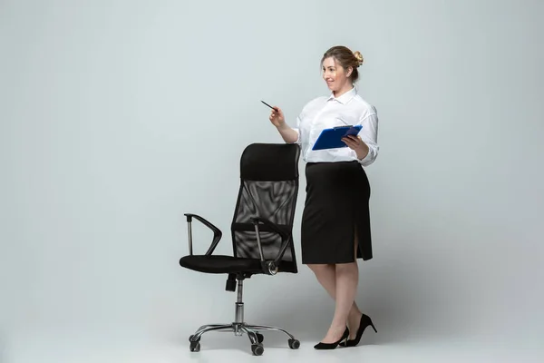 Mujer joven caucásica en traje de oficina sobre fondo gris. Personaje femenino positivo. más tamaño mujer de negocios — Foto de Stock