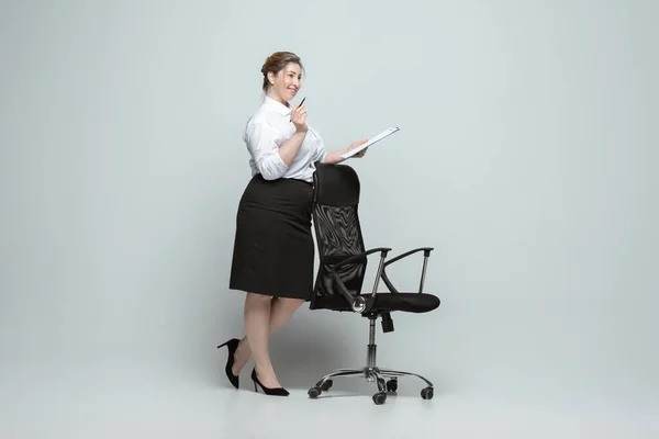 Mujer joven caucásica en traje de oficina sobre fondo gris. Personaje femenino positivo. más tamaño mujer de negocios — Foto de Stock