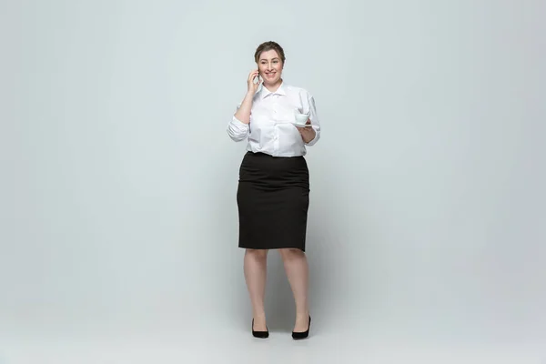 Mladá běloška v kanceláři se obléká na šedé pozadí. Tělesně pozitivní ženský charakter. plus velikost podnikatelka — Stock fotografie