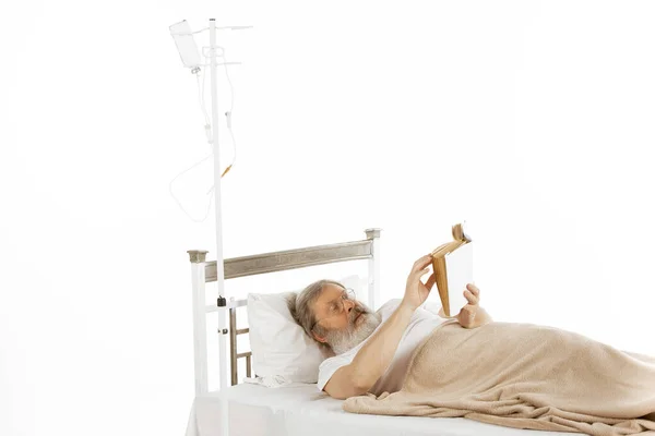 Ηλικιωμένος γέρος αναρρώνει σε ένα κρεβάτι νοσοκομείου απομονωμένο σε λευκό — Φωτογραφία Αρχείου