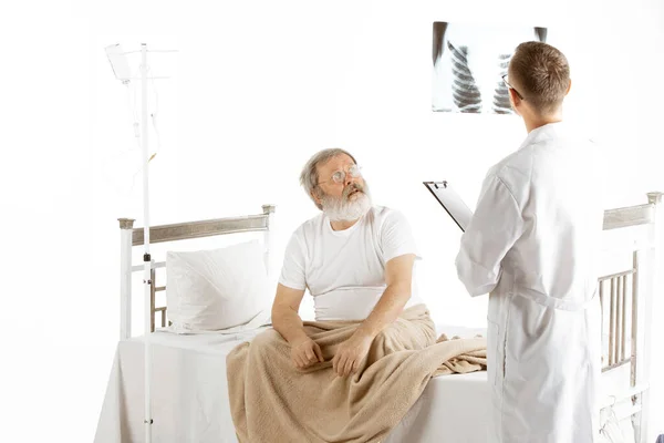 Ηλικιωμένος γέρος αναρρώνει σε ένα κρεβάτι νοσοκομείου απομονωμένο σε λευκό — Φωτογραφία Αρχείου
