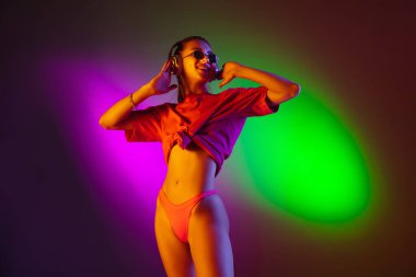 Güzel, baştan çıkarıcı bir kız, modaya uygun mayo giymiş, neon ışıklı, iki renkli stüdyo arka planında. Yaz, tatil köyü, moda ve hafta sonu konsepti