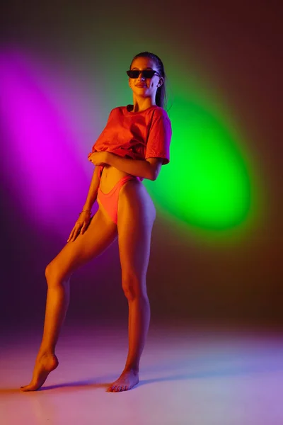 Gyönyörű csábító lány divatos fürdőruhában disco kétszínű neon stúdió háttér neon fényben. Nyár, üdülőhely, divat és hétvége koncepció — Stock Fotó