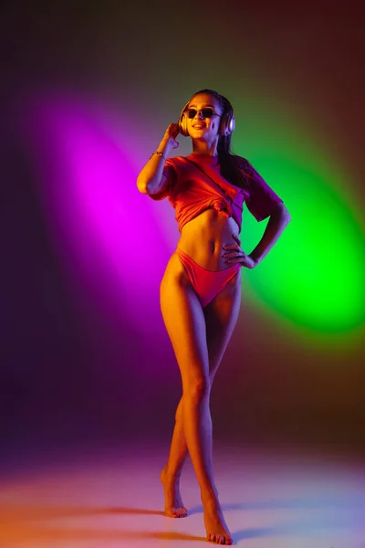 Vacker förförisk flicka i fashionabla baddräkt på disco tvåfärgad neon studio bakgrund i neon ljus. Sommar, resort, mode och helg koncept — Stockfoto