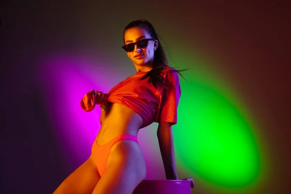 Frumoasă fată seducătoare în costum de baie la modă pe fundalul studioului de neon bicolor disco în lumina neonului. Conceptul de vară, stațiune, modă și weekend — Fotografie, imagine de stoc