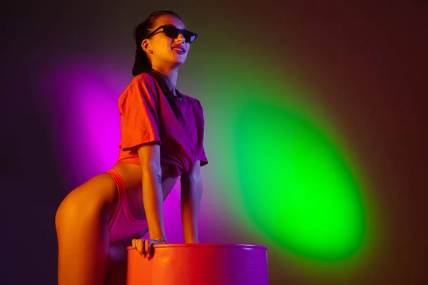 Frumoasă fată seducătoare în costum de baie la modă pe fundalul studioului de neon bicolor disco în lumina neonului. Conceptul de vară, stațiune, modă și weekend — Fotografie, imagine de stoc