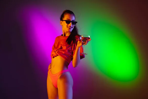 Красива спокуслива дівчина в модному купальнику на дискотечному фоні неонової студії в неоновому світлі. Літо, курорт, мода і концепція вихідних — стокове фото