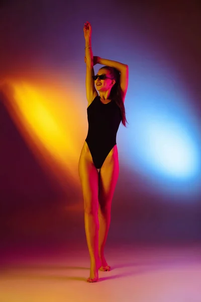 Красивая соблазнительная девушка в модном купальнике на диско-двухцветном неоновом фоне студии в неоновом свете. Концепция лета, курорта, моды и выходных — стоковое фото