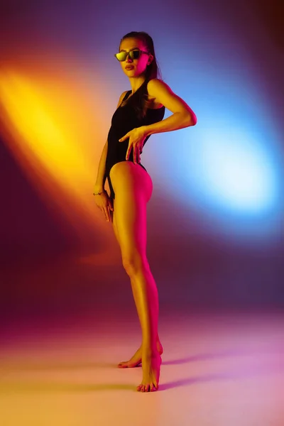 Bella ragazza seducente in costume da bagno alla moda su disco bicolore neon studio sfondo in luce al neon. Concetto estate, resort, moda e weekend — Foto Stock