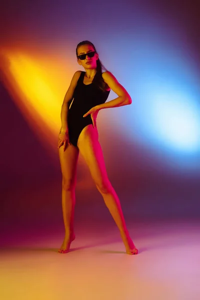 Vacker förförisk flicka i fashionabla baddräkt på disco tvåfärgad neon studio bakgrund i neon ljus. Sommar, resort, mode och helg koncept — Stockfoto