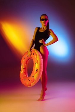 Güzel, baştan çıkarıcı bir kız, modaya uygun mayo giymiş, neon ışıklı, iki renkli stüdyo arka planında. Yaz, tatil köyü, moda ve hafta sonu konsepti