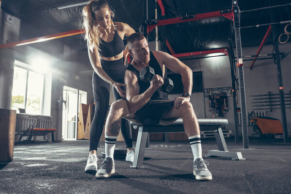 Beautiful young sporty couple training, workout in gym together