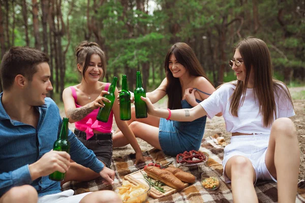 夏の森の中でピクニック中にビールボトルをクリックしている友人のグループ。ライフスタイル、友情 — ストック写真