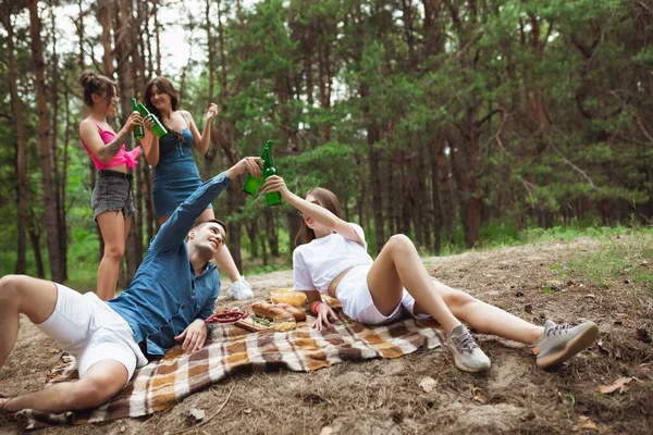 Group of friends clinking beer bottles during picnic in summer forest. Lifestyle, friendship — Stock Photo, Image