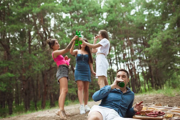 Група друзів смердить пляшками пива під час пікніка в літньому лісі. Стиль життя, дружба — стокове фото