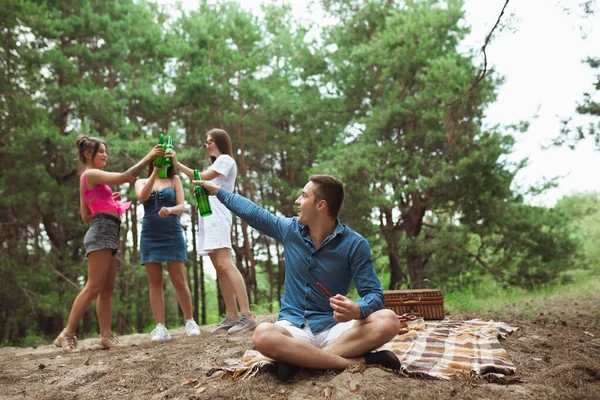 Grupo de amigos tintineando botellas de cerveza durante el picnic en el bosque de verano. Estilo de vida, amistad —  Fotos de Stock