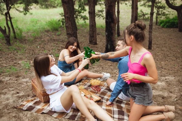 Grupa przyjaciół brzęczy butelkami piwa podczas pikniku w letnim lesie. Styl życia, przyjaźń — Zdjęcie stockowe