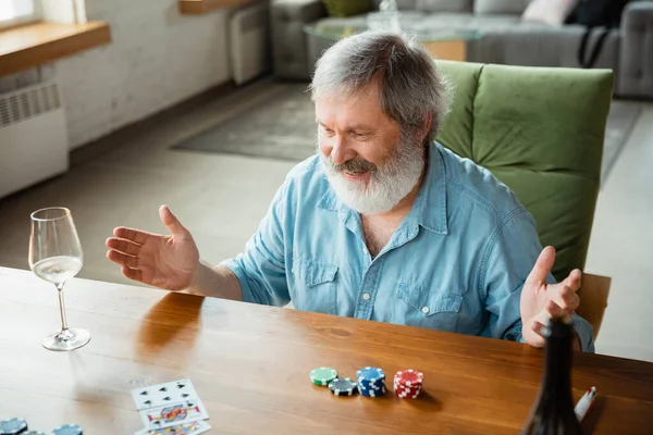 Senior man playing cards and drinking wine with friends, looks happy — Stock Photo, Image