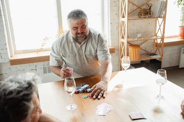 Two happy mature friends playing cards and drinking wine — Stock Photo, Image