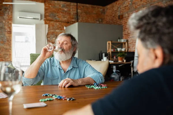 Два счастливых зрелых друга играют в карты и пьют вино — стоковое фото