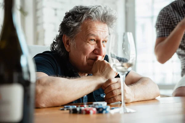 Senior man playing cards and drinking wine with friends, looks happy — Stock Photo, Image