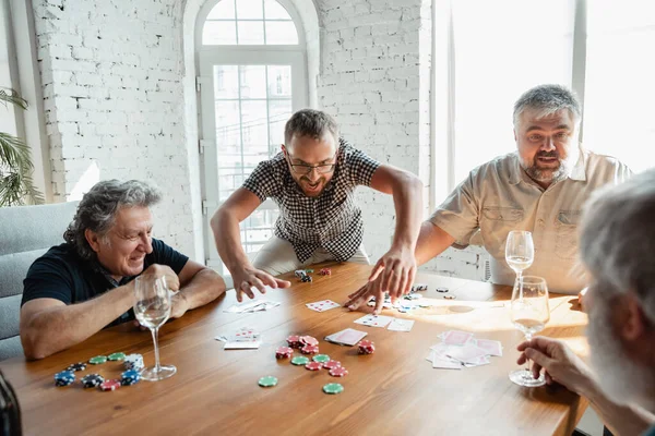 Group of happy mature friends playing cards and drinking wine — Stock Photo, Image