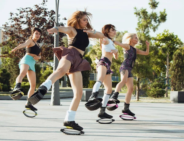 Beautiful women in sportswear jumping in a kangoo jumps shoes at the street on summers sunny day — Stock Photo, Image