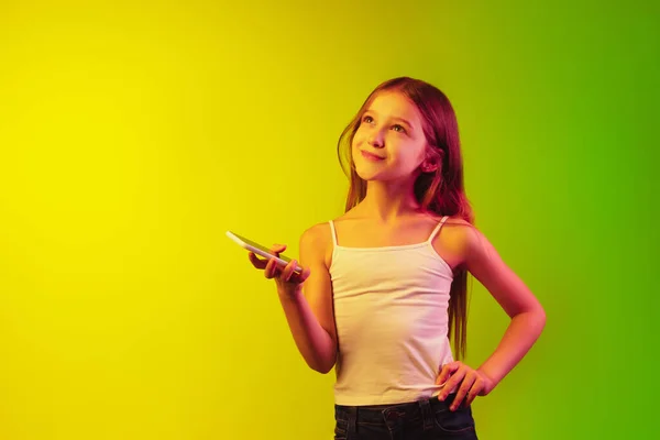 Malý kavkazský dívčí portrét izolovaný na pozadí svahu v neonovém světle. Pojem lidské emoce, výraz obličeje, moderní přístroje a technologie. Copyspace. — Stock fotografie