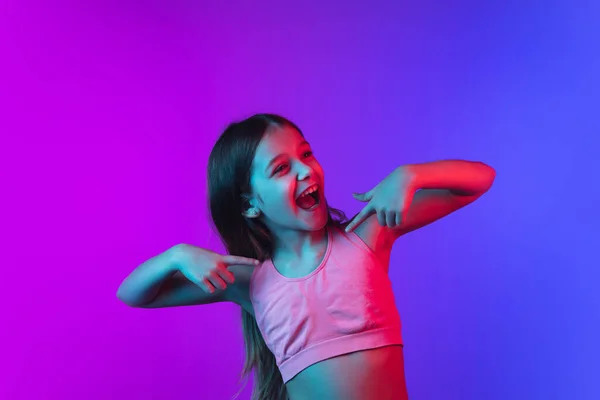 네온 빛을 받는 분홍빛 - 파란색 배경에 고립된 어린 코카서스 소녀 사진. — 스톡 사진