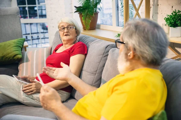 Couple of seniors spending time together being quarantined - caucasians mature and retired man and woman using modern gadgets, talking, drinking tea — Stock Photo, Image