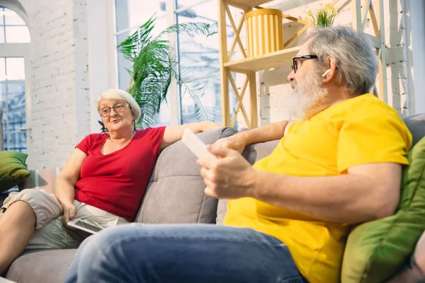 Couple of seniors spending time together being quarantined - caucasians mature and retired man and woman using modern gadgets, talking, drinking tea — Stock Photo, Image