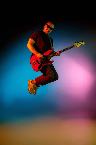 Jovem músico caucasiano tocando em fundo gradiente em luz de néon. Conceito de música, hobby, festival — Fotografia de Stock