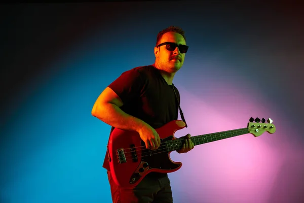 Junger kaukasischer Musiker spielt auf einem Gradienten-Hintergrund im Neonlicht. Konzept Musik, Hobby, Festival — Stockfoto