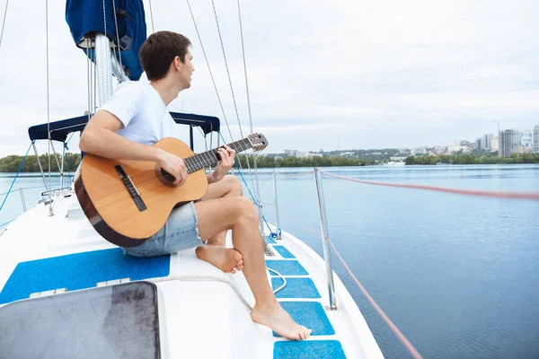 Jovem homem alegre tocando guitarra na festa de barco ao ar livre, sorrindo e feliz — Fotografia de Stock