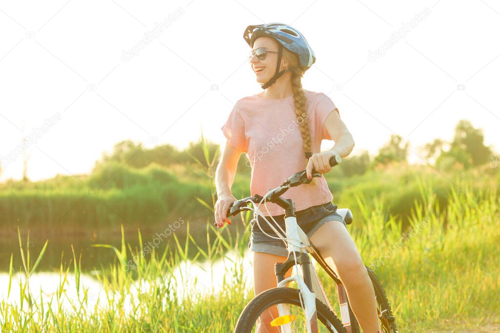 Joyful young woman riding a bicycle at the riverside and meadow promenade