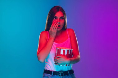 Caucasian young womans portrait isolated on gradient purple-blue background in neon light, cinema, movie watching clipart