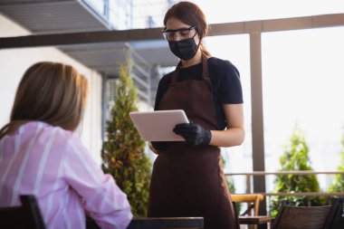 Garson, bir restoranda maske takıyor. Coronavirüs salgını sırasında eldiven takıyor.