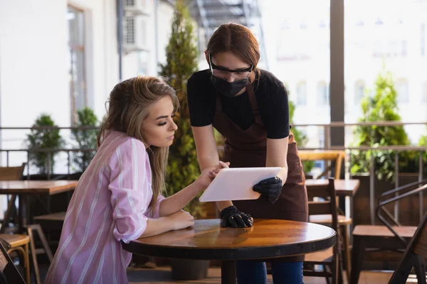 Kelnerka pracuje w restauracji w masce medycznej, rękawiczki podczas pandemii koronawirusowej — Zdjęcie stockowe