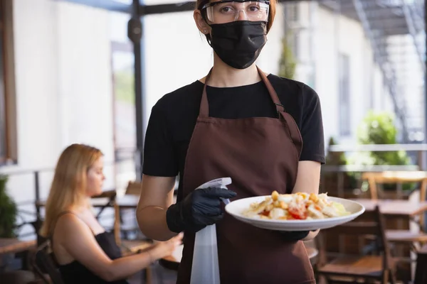 Servírka pracuje v restauraci v lékařské masce, rukavice během pandemie koronaviru — Stock fotografie