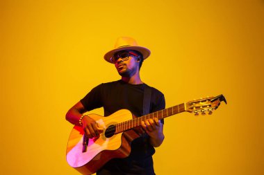 Genç Afrikalı Amerikalı müzisyen şarkı söylüyor, neon ışıkta gitar çalıyor.