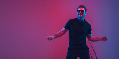 Genç beyaz müzisyen şarkı söylüyor, neon ışıkta dans ediyor, el ilanı dağıtıyor.