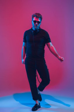 Genç beyaz müzisyen şarkı söylüyor, neon ışıkta dans ediyor.