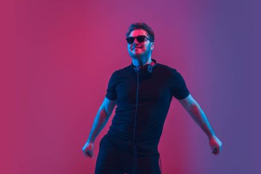 Genç beyaz müzisyen şarkı söylüyor, neon ışıkta dans ediyor.