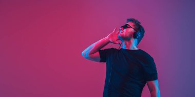 Genç beyaz müzisyen şarkı söylüyor, neon ışıkta dans ediyor, el ilanı dağıtıyor.