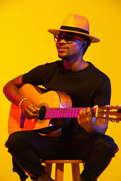 Joven músico afroamericano cantando, tocando la guitarra en luz de neón — Foto de Stock