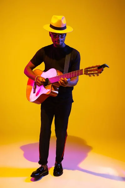 Joven músico afroamericano cantando, tocando la guitarra en luz de neón — Foto de Stock