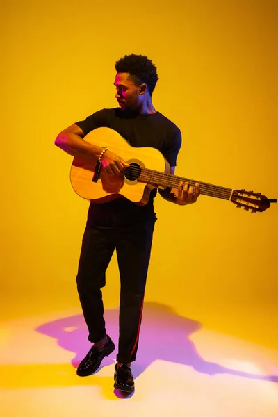 Jovem músico afro-americano cantando, tocando guitarra em luz néon — Fotografia de Stock